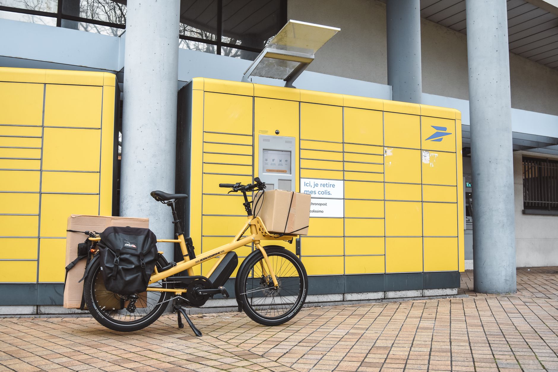 Ciclista che sistema la cargo e-bike vicino a un muretto in pietra in un centro storico