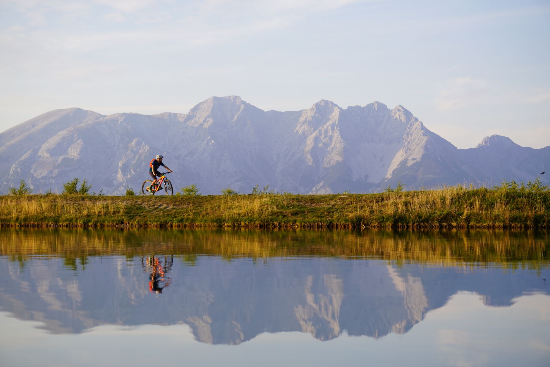 Cyclist riding an e-bike along a lakeside road with alpine mountains in the background