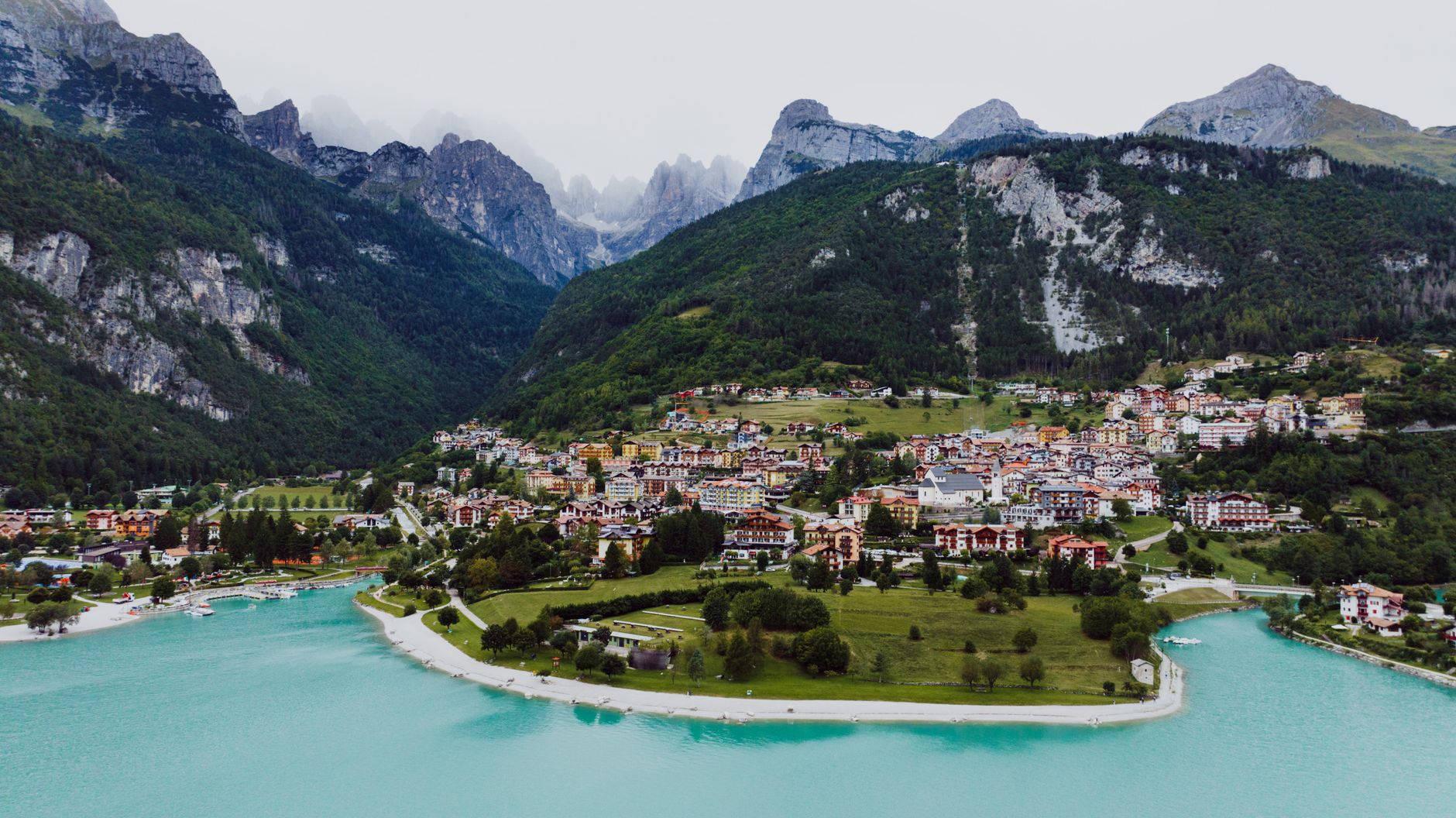 Cyclist riding an e-bike along a lakeside road with alpine mountains in the background